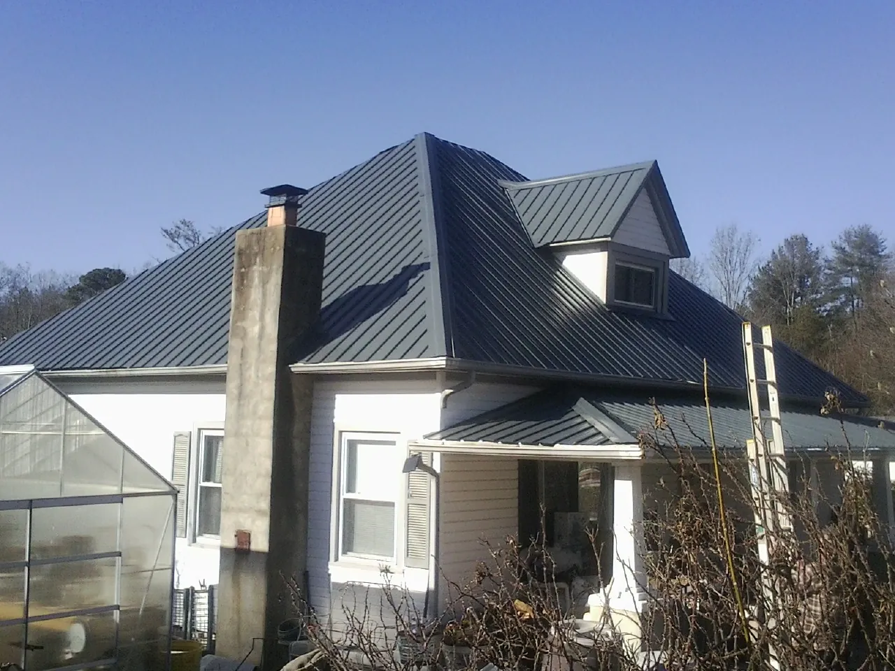 Dark blue standing seam metal roof on a white farmhouse with dormer — Slate & Tile Roof Repair by Roofing Brothers in Grenloch