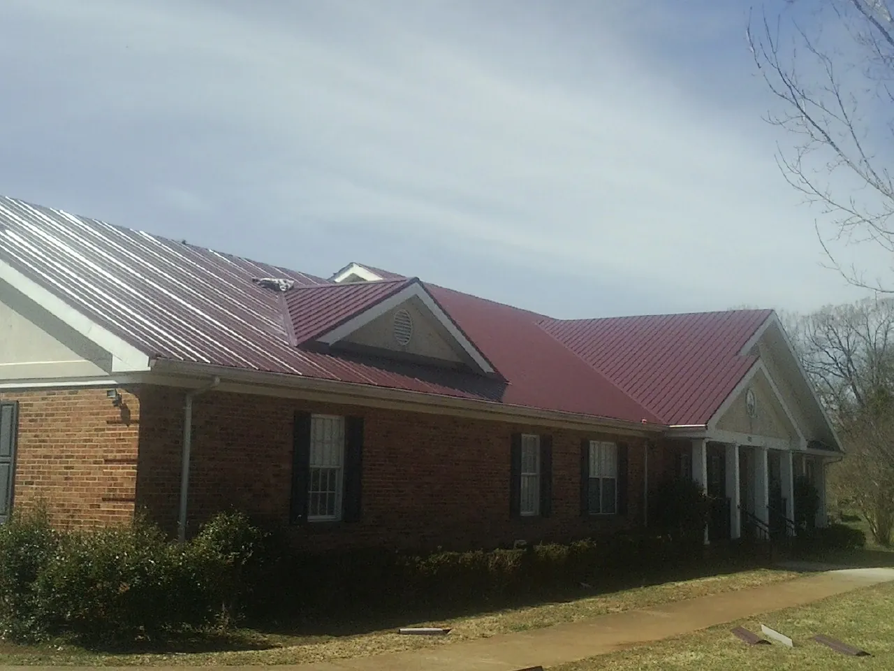 Red metal roof with gabled entries on a long brick building, from a Hail Damage Roof Repair job in Grenloch
