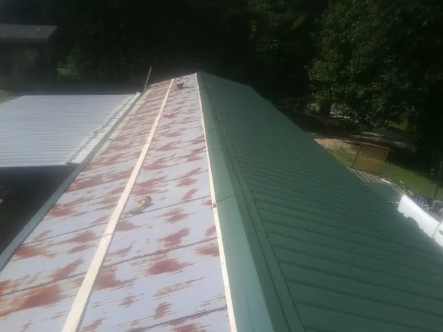 Old rusted panels beside newly installed green metal roofing — Wind Damage Roof Repair by Roofing Brothers in Grenloch