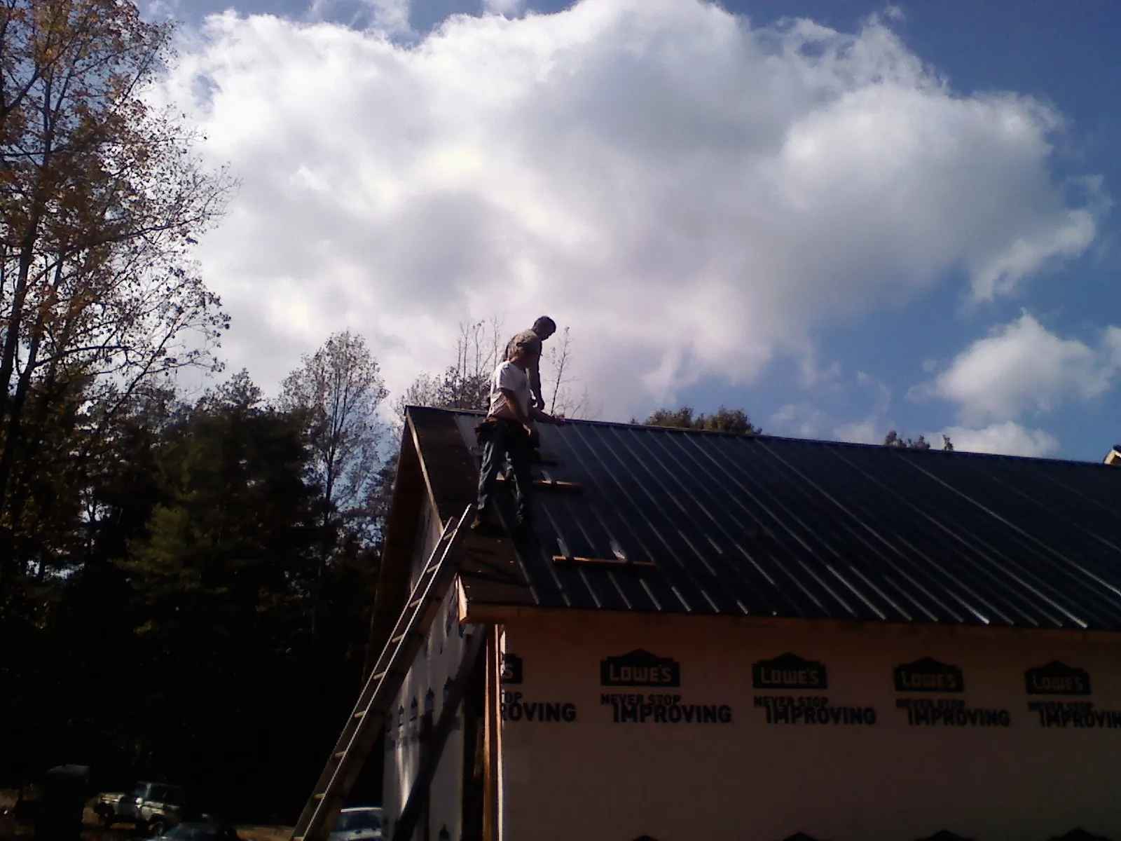 Roofer fastening dark metal panels high against a cloudy sky, from a Roof Inspection job in Grenloch