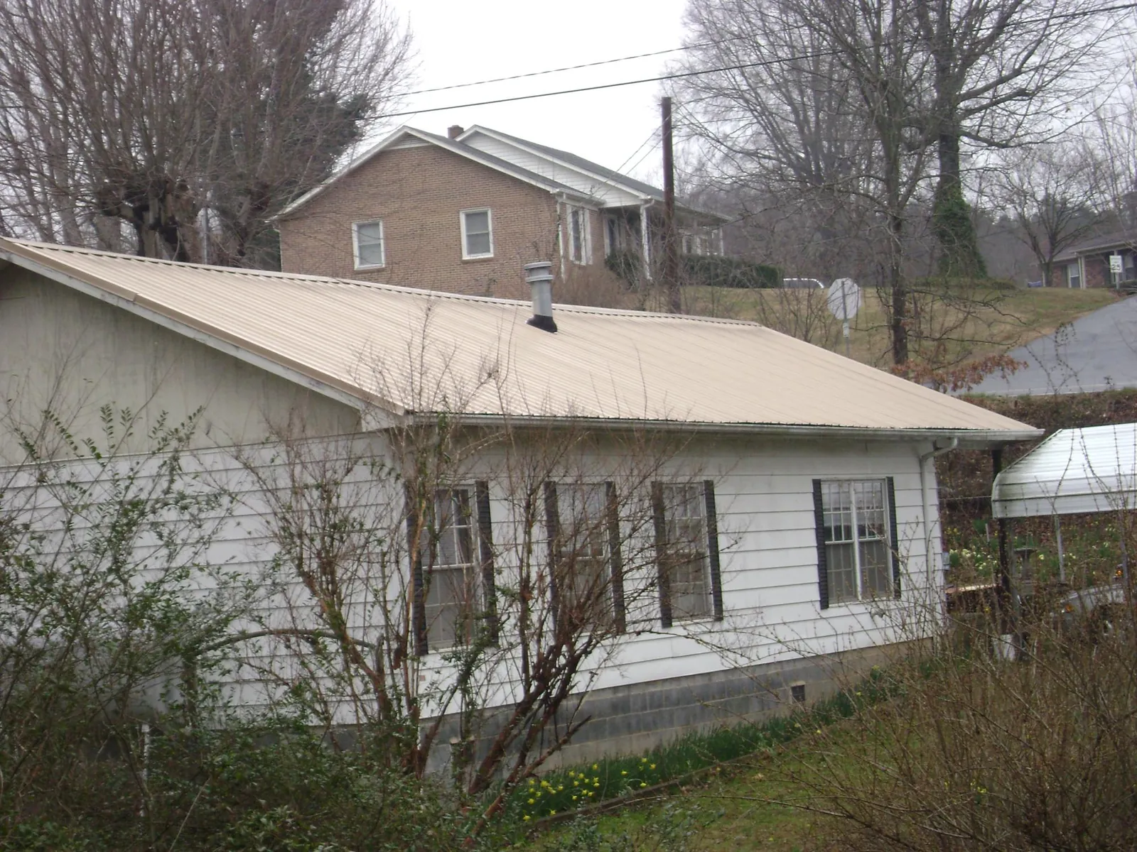 Tan metal roof on a white sided house set into a hillside — Commercial Roofing by Roofing Brothers in Grenloch