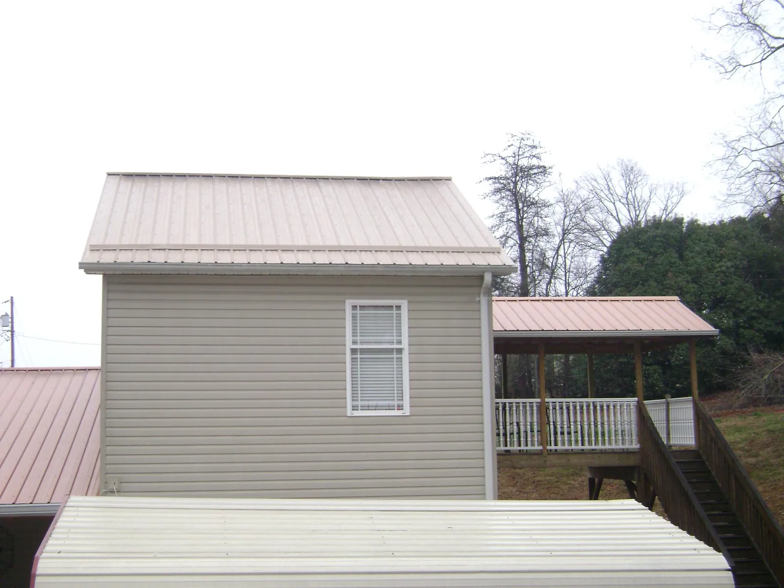 Tan metal roofs on a two story addition and attached porch, from a Roof Replacement job in Grenloch